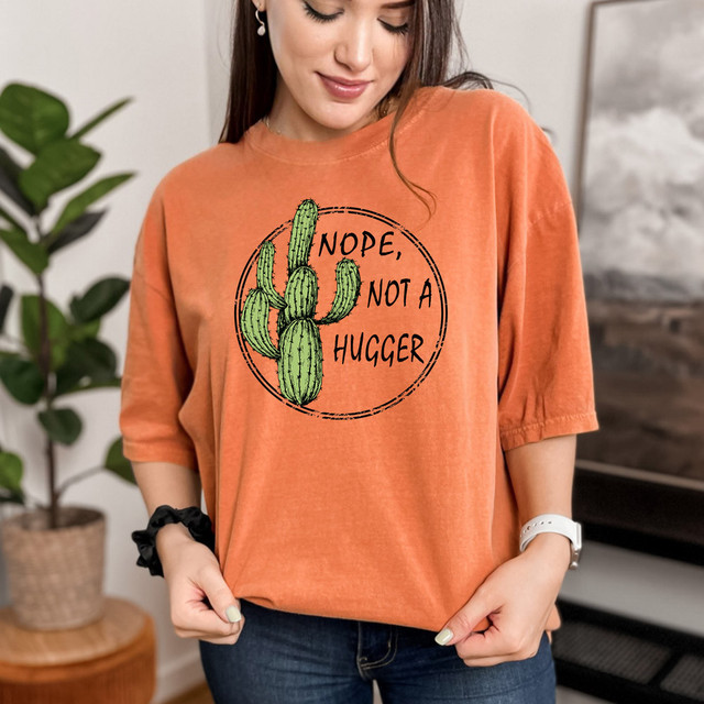 Not A Hugger DTF Heat Transfer, graphic of a cactus and the text 'Nope, Not A Hugger' on an orange T-shirt worn by a woman.