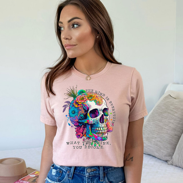 The Mind Is Everything DTF Heat Transfer, colorful skull design with flowers and the quote 'The mind is everything. What you think, you become' on a woman's pink t-shirt.