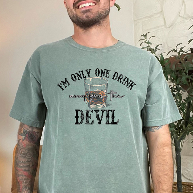 One Drink Away DTF Heat Transfer, a design featuring a glass of whiskey with the text 'I'm only one drink away from the devil' printed on a green t-shirt.