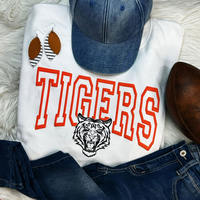 Tigers Orange PUFF Screen Print Heat Transfer, vibrant orange and black tiger logo on white fabric with 'TIGERS' text, displayed with jeans, denim cap, brown shoes, and earrings.