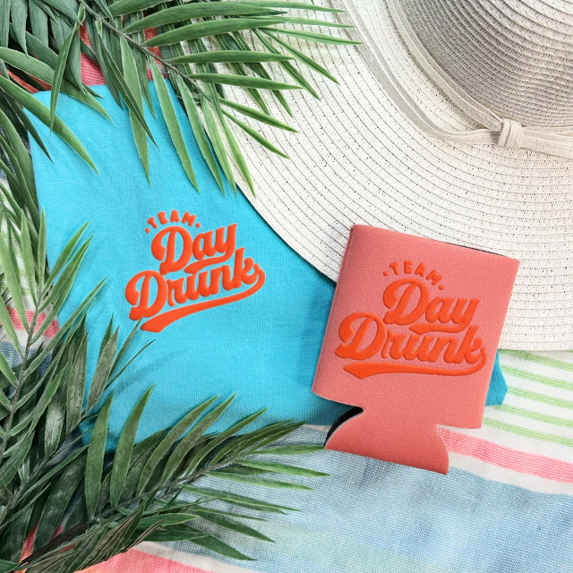 Team Day Drunk Orange PUFF Pocket Screen Print Heat Transfer, close-up of vibrant orange heat transfer design on a blue fabric with beach accessories in background.