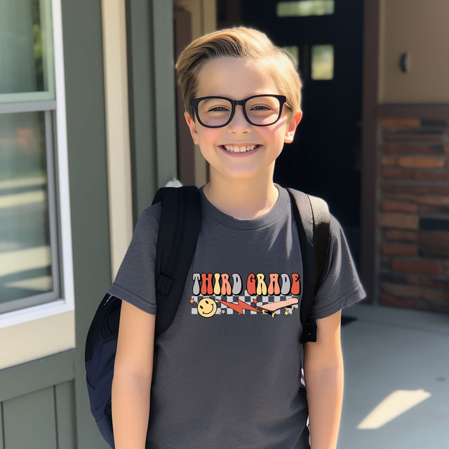 Third Grade Lightning Bolt DTF Heat Transfer, a colorful graphic design on a dark gray T-shirt worn by a smiling schoolboy.