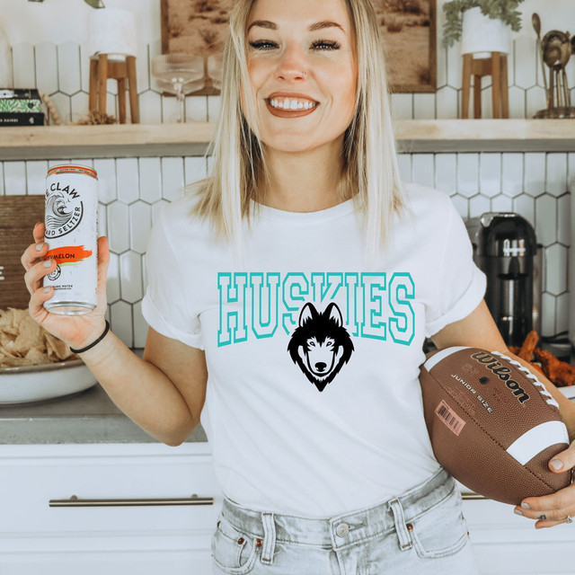 Huskies *CUSTOM COLOR OPTIONS* DTF Heat Transfer latest style, woman holding a can of sparkling water and a football, wearing a white t-shirt with a huskies graphic, in a modern kitchen.