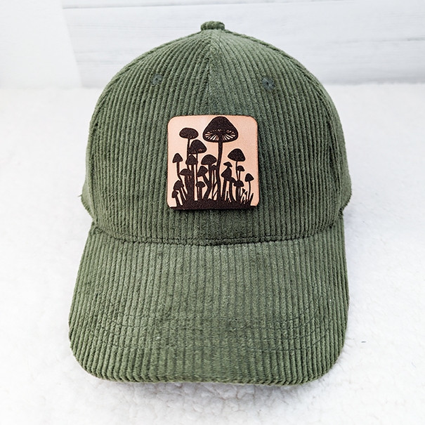 Mushroom Leather Hat Patch, forest green corduroy baseball cap with mushroom graphic patch on front.