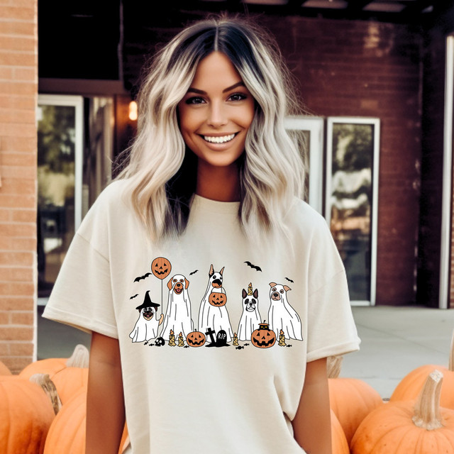 Dog Ghosts DTF Heat Transfer, woman wearing a Halloween-themed t-shirt with illustrated ghost dogs dressed in costumes and surrounded by pumpkins and bats.