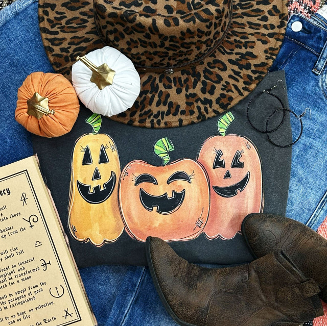 Three Pumpkins Screen Print Heat Transfer, colorful Halloween pumpkin designs with smiling faces on black fabric, with Halloween-themed accessories and clothing around.