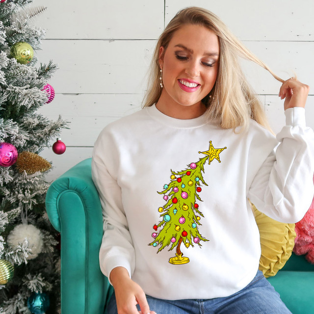 Little Tree DTF Heat Transfer, Christmas tree with colorful ornaments and star on top, on a woman's sweatshirt near a decorated Christmas tree.