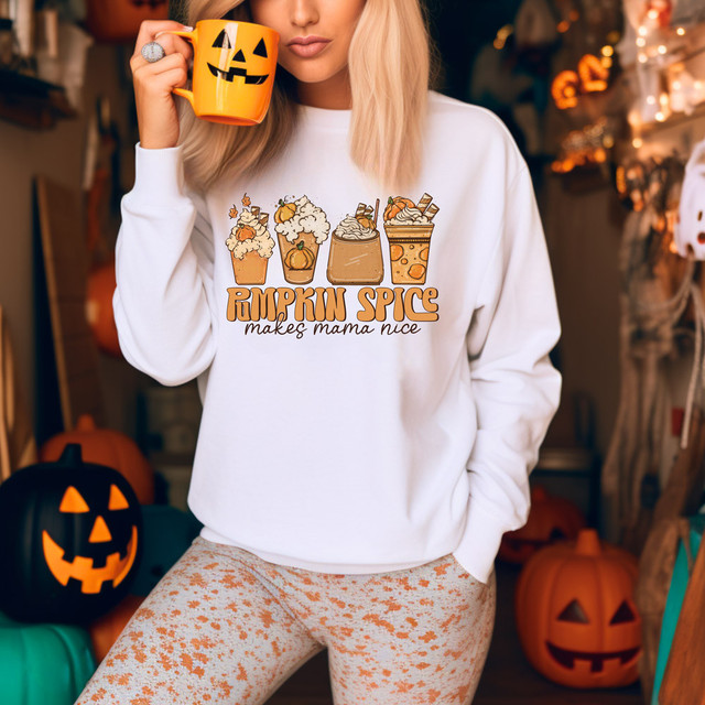 Pumpkin Spice Makes Mama Nice DTF Heat Transfer, close-up of a woman wearing a white sweatshirt with pumpkin spice beverage graphics and text, holding a pumpkin-themed mug, Halloween decorations in the background.