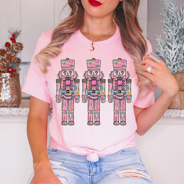 Watercolor Nutcrackers DTF Heat Transfer, colorful nutcracker design on a pink T-shirt worn by a woman in a festive holiday setting.