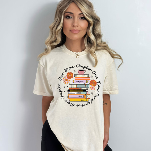 One More Chapter DTF Heat Transfer, illustrated design on a woman's cream t-shirt featuring stacked books with flowers and text