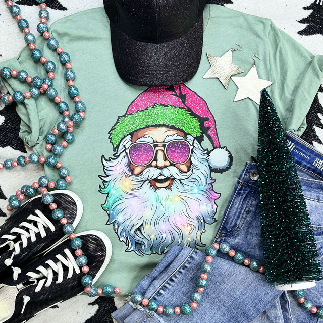 Stylin' Santa Screen Print Heat Transfer, colorful holiday-themed design featuring Santa Claus wearing sunglasses and a Christmas hat, laid out on a green t-shirt surrounded by Christmas accessories.