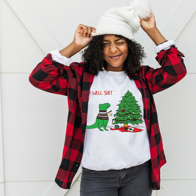Well Shit TRex DTF Heat Transfer, a humorous Christmas-themed graphic featuring a dinosaur and a decorated Christmas tree on a white T-shirt.