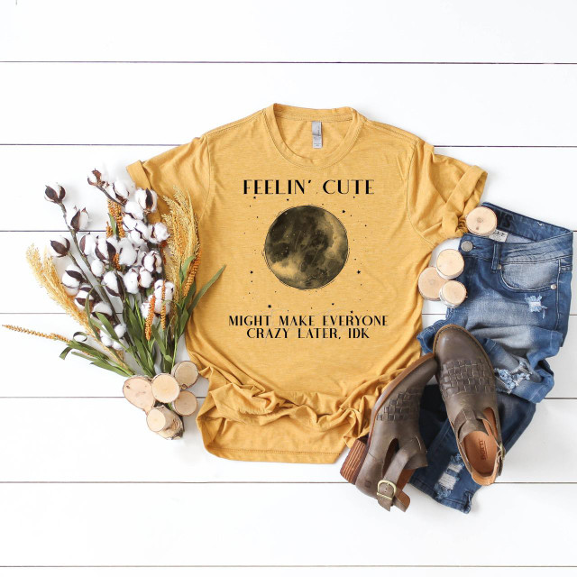 Full Moon Feelin Cute May Make Everyone Crazy Later, IDK Sublimation Transfer T-Shirt, yellow graphic tee with moon design and humorous text, displayed with denim shorts, brown shoes, and cotton bouquet on white wooden background.