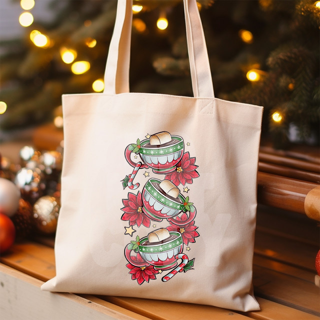 Festive Hot Cocoa DTF Heat Transfer, cheerful holiday design featuring three mugs of hot cocoa with marshmallows, poinsettias, candy canes, holly leaves, and stars on a tote bag.