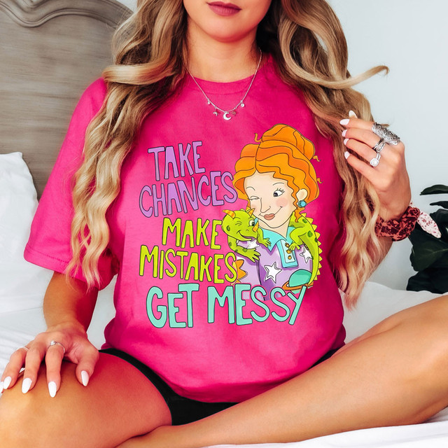 Take Chances Make Mistakes Get Messy DTF Heat Transfer, colorful woman wearing a pink T-shirt with playful graphic and text, sitting on bed.