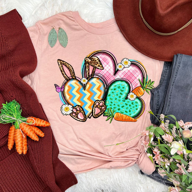 Easter Hearts DTF Heat Transfer, colorful Easter-themed heart designs with bunny ears, carrots, daisies, and vibrant patterns on a pink T-shirt.