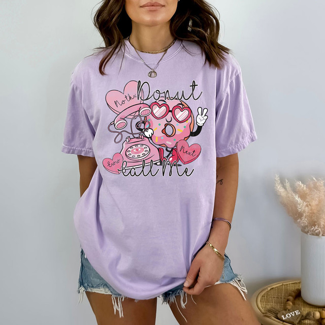 Donut Call Me DTF Heat Transfer, shown on a woman's lavender T-shirt featuring a playful donut graphic with heart-shaped sunglasses and colorful sprinkles.