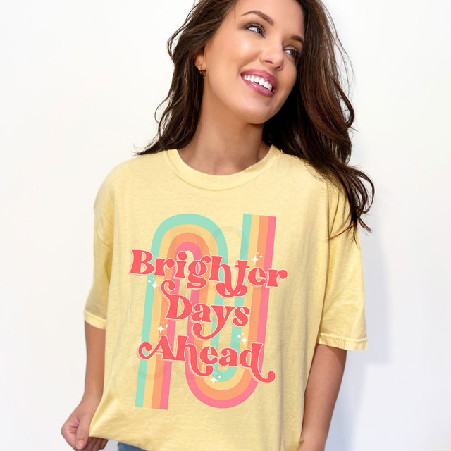 Brighter Days Ahead DTF Heat Transfer, colorful retro rainbow design with uplifting text on a yellow t-shirt worn by smiling woman.