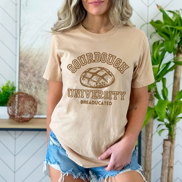 Sourdough University DTF Heat Transfer, beige t-shirt with sourdough bread graphic and university text, worn by a woman in casual denim shorts.