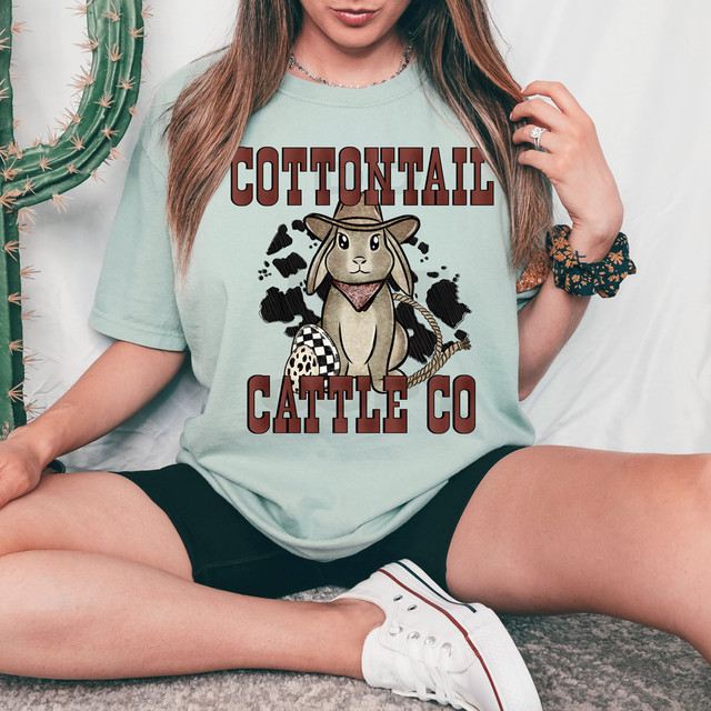 Cottontail Cattle Co DTF Heat Transfer, a graphic design of a cartoon rabbit wearing a cowboy hat, bandana, and saddle, with bold text 'Cottontail Cattle Co' in front of a black splatter background.