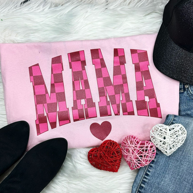 MAMA Checkered SHIMMER Screen Print Heat Transfer, pink checkered 'MAMA' text design on a light pink shirt displayed with black shoes, a black cap, a pair of jeans, and decorative heart-shaped wicker balls.