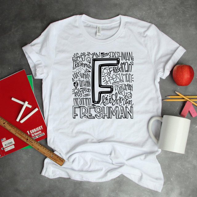 Freshman Typography Word Art Sublimation Transfer, white T-shirt with black graphic and text design featuring the letter F and the word 'FRESHMAN' surrounded by school-related doodles and words.