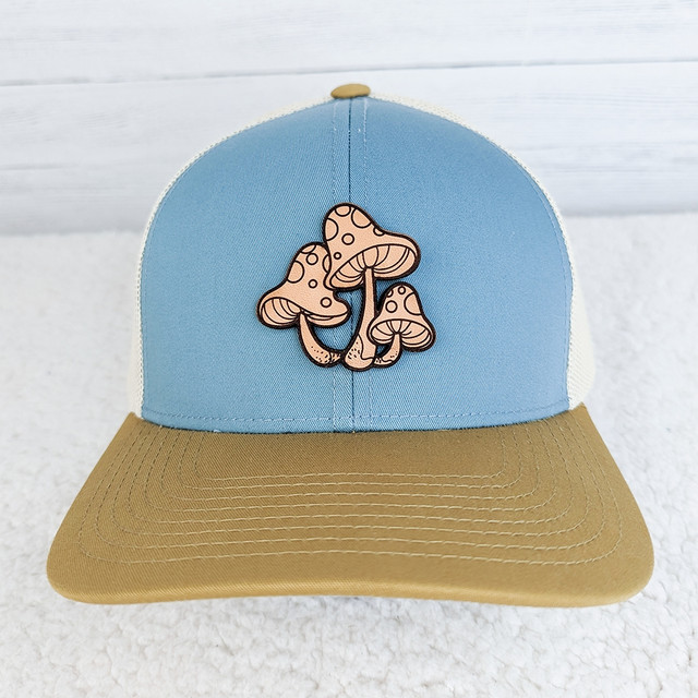 Mushrooms Leather Hat Patch, embroidered patch of three stylized mushrooms with spots on a blue and beige trucker cap.