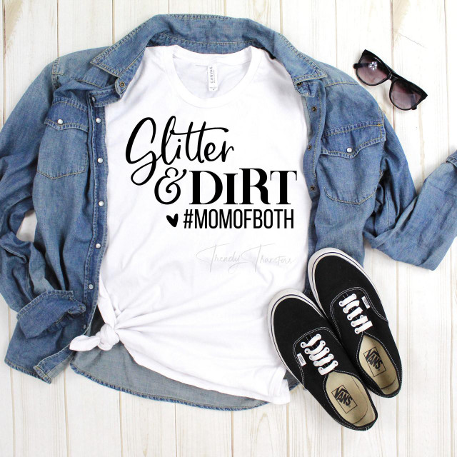 Glitter and Dirt Mom of Both Sublimation Transfer, product image of a white T-shirt with black and cursive print, layered under a denim jacket, with black Vans sneakers and sunglasses on a white wooden background.