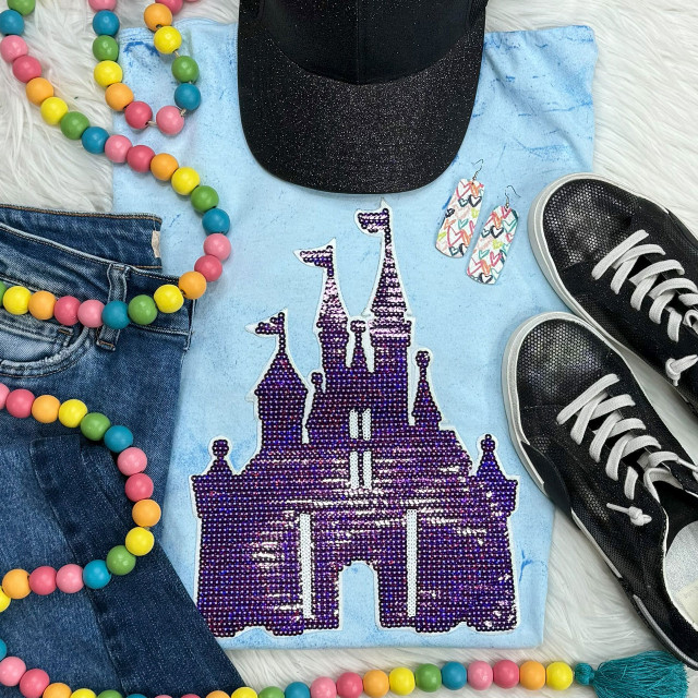 Purple Castle Sequin Patch, a purple sequin appliqué of a castle on a light blue fabric with various colorful accessories including a beaded necklace, denim jeans, a black glittery cap, and black sneakers.