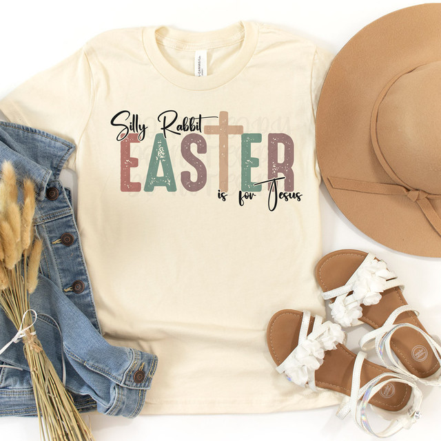 Silly Rabbit Easter Is For Jesus Cross DTF Heat Transfer, graphic t-shirt design with pastel-colored text reading 'Silly Rabbit Easter Is For Jesus' arranged on a cream t-shirt, paired with a beige hat, denim jacket, and white sandals with floral accents.