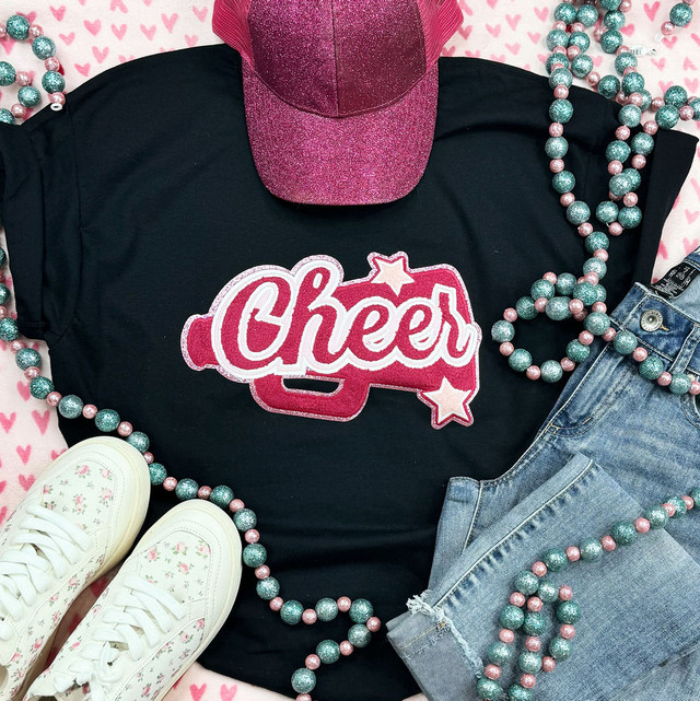 Cheer Megaphone Pink Chenille Patch, pink and glittery cheer megaphone patch on a black T-shirt with the word Cheer, pink and blue beaded necklaces, pink baseball cap, distressed denim jeans, and white sneakers with pink floral patterns