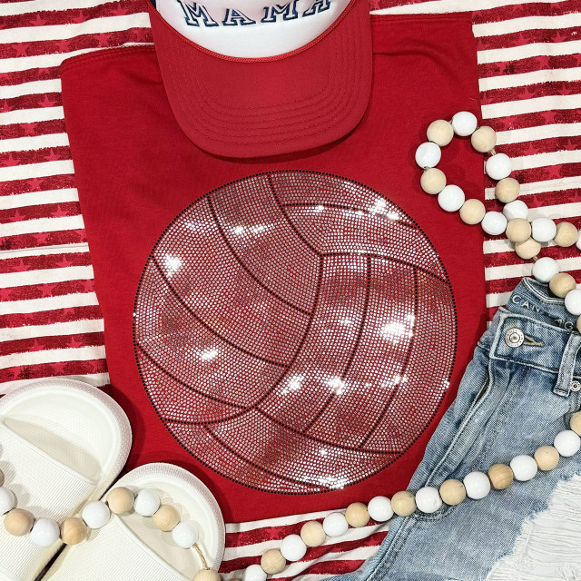 Spangled VOLLEYBALL Transfer, a glittery red T-shirt with a volleyball graphic design, paired with a red cap, denim shorts, white shoes, and a beaded necklace, laid out on a striped red and white background.