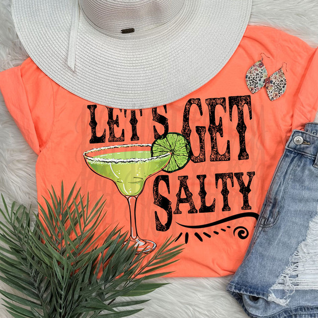 Let's Get Salty DTF Heat Transfer, vibrant orange t-shirt with a lime margarita glass graphic and the slogan 'Let's Get Salty', paired with a large sunhat, floral earrings, and denim shorts.