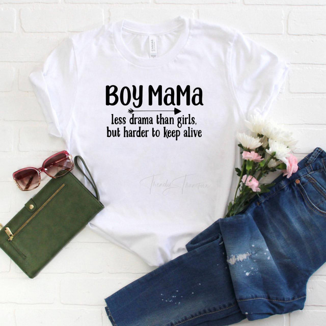 Boy MaMa Less Drama Than Girls But Harder to Keep Alive Sublimation Transfer - White T-Shirt with black text and arrow design, surrounded by sunglasses, a green clutch, denim jeans, and pink and white flowers.