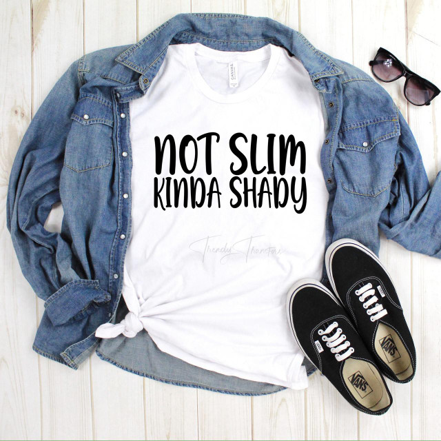 Not Slim Kinda Shady Sublimation Transfer, white T-shirt with black text displayed flat with jeans jacket, black Vans sneakers, and sunglasses on a wooden surface.