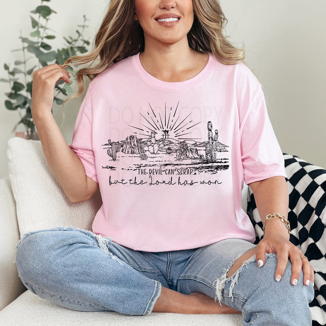 The Devil Can Scrap DTF Heat Transfer, a woman wearing a pink T-shirt with a desert landscape and sunburst design with the quote 'the devil can scrap but the Lord has won'