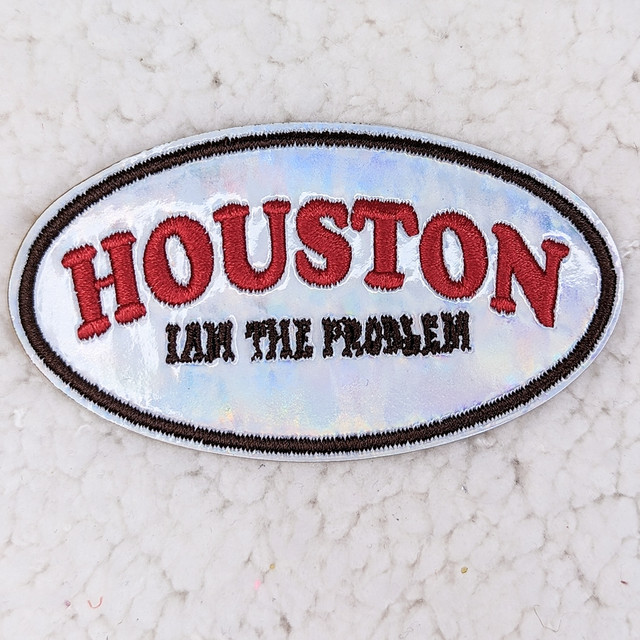 Houston I Am The Problem Embroidered Vinyl HAT/POCKET Patch, oval patch with red embroidered text and black embroidered phrase, reflective vinyl background, black border.