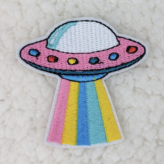 UFO Embroidered HAT/POCKET Patch, colorful embroidered UFO with rainbow-colored beams on a white fabric background.