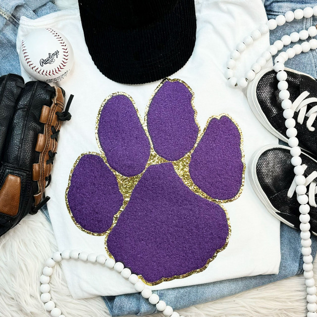 Purple Paw with Gold Glitter Chenille Patch, a decorative purple paw print patch featuring gold glitter accents, placed on a white fabric background surrounded by sneakers, a baseball, a black hat, and white bead necklaces.