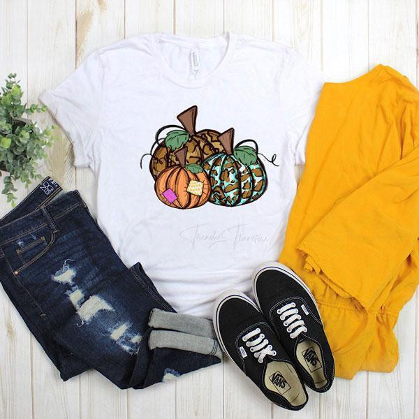 Patchwork Fall Pumpkins Sublimation Transfer, graphic t-shirt with colorful pumpkin design and fall-themed patchwork, paired with denim jeans, yellow pants, and black sneakers.
