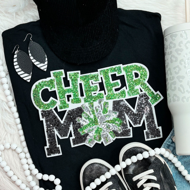 Green Sequin Cheer Mom Patch, a decorative patch with shiny green sequins spelling 'CHEER MOM' with a bow design, on a black shirt surrounded by cheer accessories.