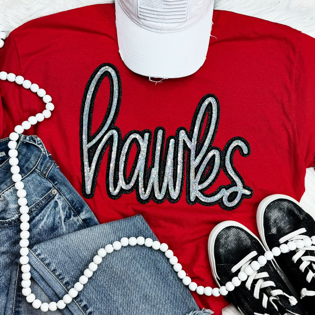Hawks Sequin Patch, sparkling black and white sequin patch spelling 'Hawks' on a red t-shirt, casual outfit with denim jeans and black sneakers, accessorized with white beaded necklace and a white cap.