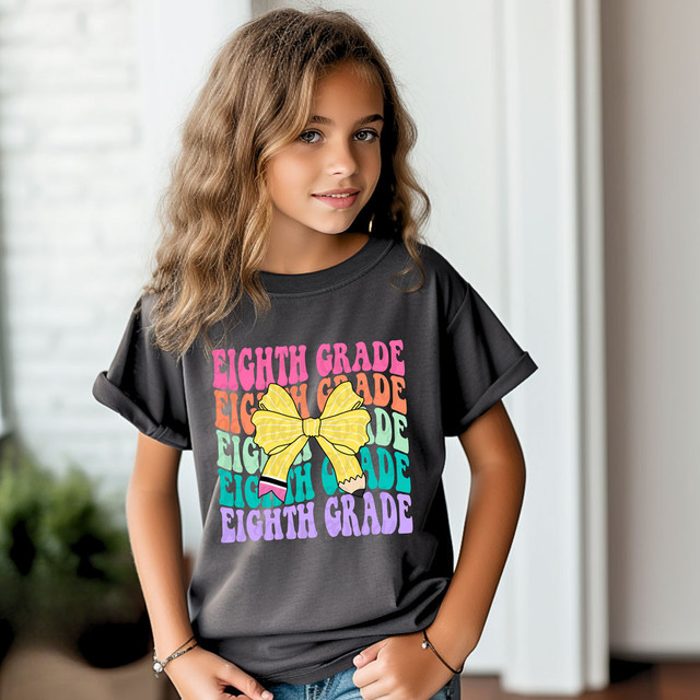 Eighth Grade Coquette Pencil Bow DTF Heat Transfer, a colorful heat applied design featuring repeated phrases 'Eighth Grade' and a yellow bow on a girl's dark T-shirt.