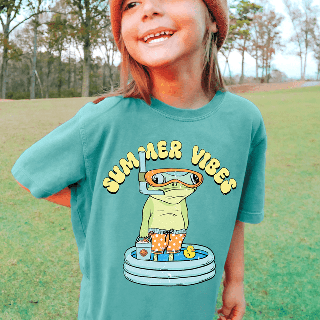 Summer Vibes Frog DTF Heat Transfer, colorful cartoon frog wearing snorkeling gear and swimsuit, standing with pool float, on a teal t-shirt, summer fun and water activity theme.