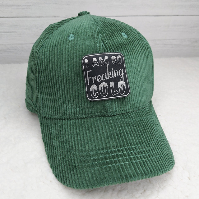 I Am So Freaking Cold FAUX Leather Patch, green corduroy baseball cap with a black patch embroidered with white text.