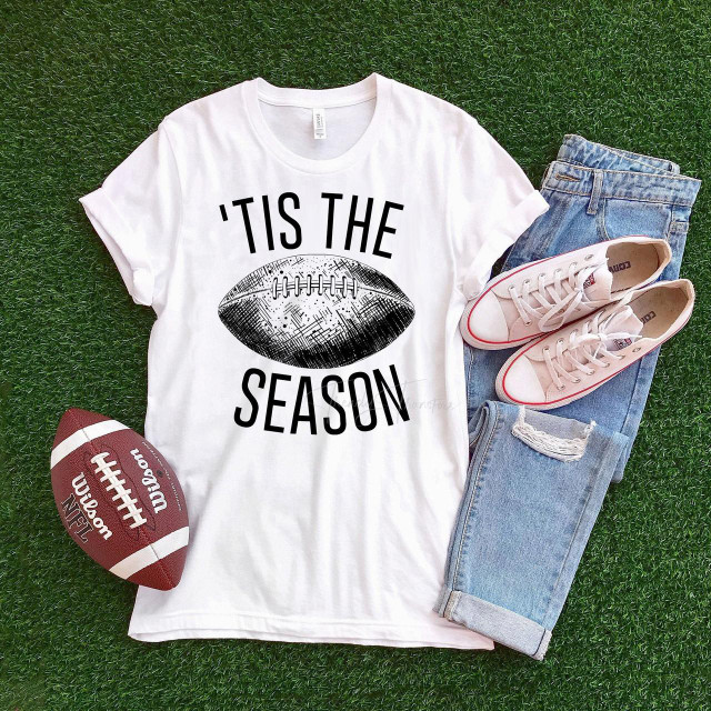 Tis the season Football Sublimation Transfer, a graphic T-shirt with a football design and text, casual sneakers, ripped jeans, and a football on green grass.