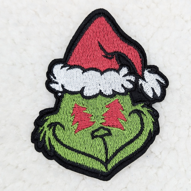 Grouchy Green Guy Embroidered HAT/POCKET Patch, a colorful patch featuring a green character with a Santa hat and red tree-shaped eyes, smiling.