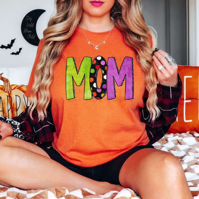 Mom Halloween Letters DTF Heat Transfer, colorful and patterned Halloween-themed text design on a women's orange T-shirt.