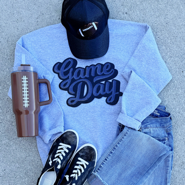 Sequins Navy Game Day Patch, navy blue sequins football-themed patch on a gray sweatshirt with 'Game Day' text, paired with a black football cap, black sneakers, distressed jeans, and a brown tumbler with a white stripe.