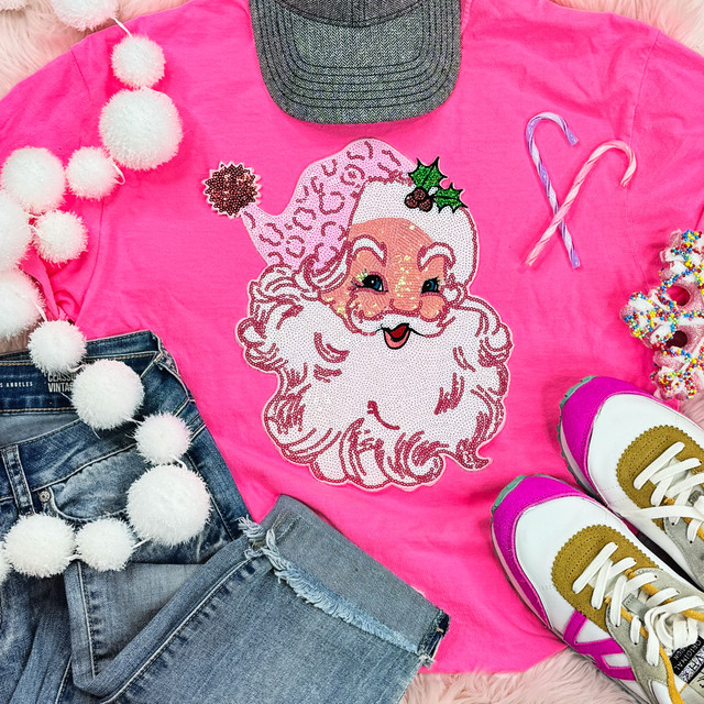 Sequins Pink Santa Patch, close-up of a pink sweatshirt featuring a sequin Santa Claus face with a holly decoration, surrounded by Christmas-themed accessories including pom-pom garland, candy canes, colorful sprinkles, and pink sneakers.